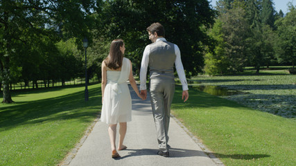Fototapeta premium CLOSE UP: Young happy couple holding hands gaze at each other walking in park