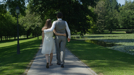Fototapeta premium CLOSE UP: Blissful embraced pregnant couple strolling through park on sunny day
