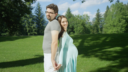 Fototapeta premium CLOSE UP: Pregnant couple standing side by side in beautiful park on sunny day
