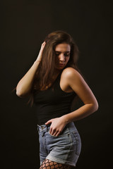 Model test with glamor young model in black shirt and jeans shorts posing in the shadows