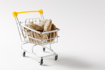 Close up of supermarket grocery push cart for shopping with yellow plastic elements on handle filled with brown stones isolated on white background. Concept of shopping. Copy space for advertisement