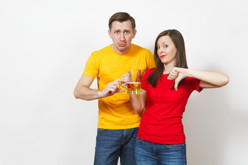 Obraz premium Sad upset crying young couple woman, man, football fans in yellow red t-shirts with pint mug of little beer ends show thumb down isolated on white background. Sport, family leisure, lifestyle concept.