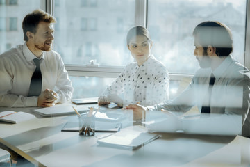 Detailed report. Two young colleagues sitting at the table in the office of their boss and reporting him while he paying attention
