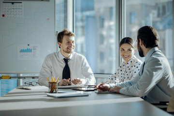 Pleasant conversation. Upbeat young colleagues sitting at the table during the meeting and chatting cheerfully with each other while smiling