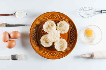 Raw pasta in plate and ingredients, flour, eggs, yolk, knife, rolling pit, spoon.