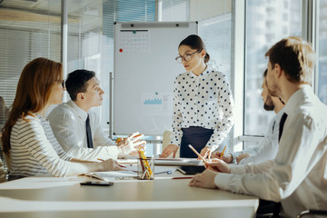 Quick instruction. Charming young female boss answering the questions of her colleagues related to job issues while having a morning briefing with them