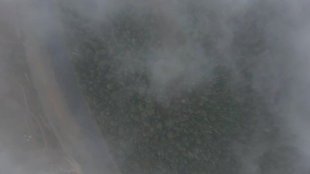 Aerial tracking shot of mountain river flowing between the mountains covered with forest. Gray rain clouds. Fog over the river.