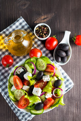 Fototapeta na wymiar Fresh Greek salad made of cherry tomato, ruccola, arugula, feta, olives, cucumbers, onion and spices. Caesar salad in a white bowl on wooden background. Healthy organic diet food concept.
