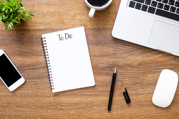 Notebook with to do text on it over wood office desk table with supplies. Top view, flat lay.