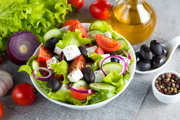 Fresh Greek salad made of cherry tomato, ruccola, arugula, feta, olives, cucumbers, onion and spices. Caesar salad in a white bowl on wooden background. Healthy organic diet food concept.