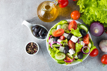 Fresh Greek salad made of cherry tomato, ruccola, arugula, feta, olives, cucumbers, onion and spices. Caesar salad in a white bowl on wooden background. Healthy organic diet food concept.
