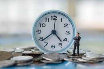 Global, Time and Business concept. Businessman miniature figures standing on pile of coins with vintage round clock.