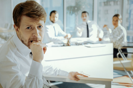 In Trouble. Agitated Young Manager Sitting At The Meeting With The Board Of Directors And Biting His Finger, Being In Stress