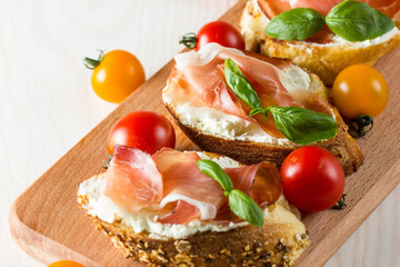 Italian tomato, prosciutto, jamon, ham and cheese bruschetta. Tapas, antipasti with chopped vegetables, herbs and oil on grilled ciabatta and baguette bread.