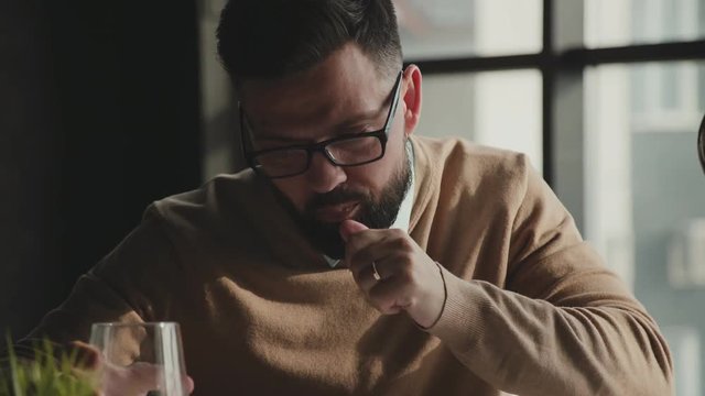 Hipster businessman with beard suffering headache, taking painkillers at workplace. A young male businessman takes a pill at the workplace. A young man takes care of his health and takes vitamins.