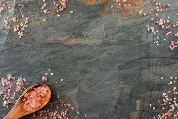 Frame of pink Himalayan salt with spoon. Top view on a dark stone background.