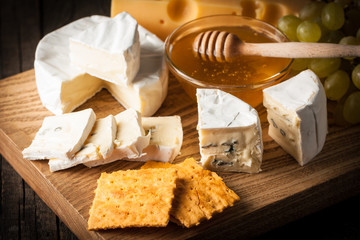 Slate board with various cheese and a glass of red rose wine. Brie. Camembert. Gouda, Masdaam, Roquefort, Cheddar and grapes on a wood with nuts, honey, crackers, blue cheese. Italian, French cheese.