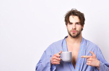 Macho with strict face in bathrobe points at mug.
