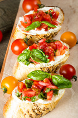 Tomato and cheese fresh made bruschetta. Italian tapas, antipasti with vegetables, herbs and oil on grilled ciabatta and baguette bread.
