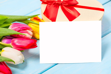 Colorful spring tulip flowers with decorative giftbox and blank photo on light blue wooden background as greeting card. Mothersday or spring concept.
