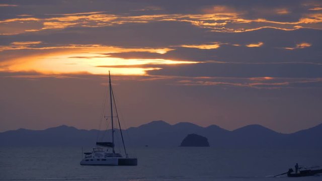 Yacht catamaran on the roadstead with a floating long-tail boat in foreground at sunset