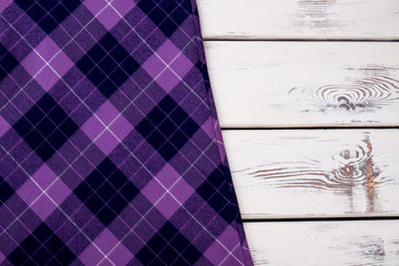Purple violet checkered plaid clothes material. Close up macro view. White wooden desks surface background.