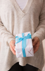 Closeup of young girl's hands holding nicely wrapped in white paper and decorated with blue ribbon Christmas, birthday or any other celebration gift.