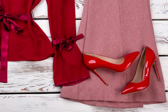 Close up red pair of heel shoes on clothes. Silk and cotton dresses. White wooden desks surface background.