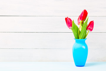 Colorful red spring tulip flowers in nice blue vase on light wooden background as greeting card. Mothersday or spring concept