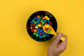 Top view of right hand holding yellow spoon over a black bowl of candy
