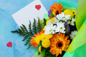 A wedding story or background Mother's Day. Bouquet of gerbera with chrysanthemums and sweets on a blue stone background or concrete. Free space for your congratulations, top view flat lay background.