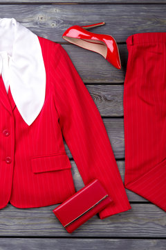 Red feminine suit, shoe and wallet. Flat lay, grey wooden surface background.