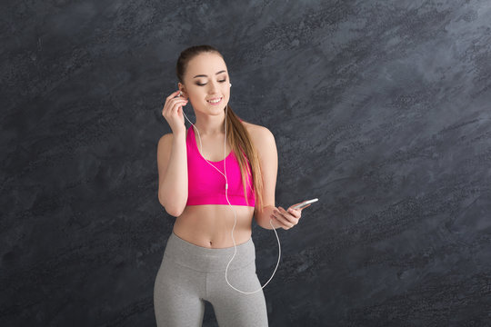 Fitness girl in earphones listening music on smartphone