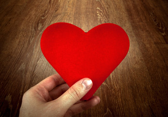 symbol of a red heart on a wooden background in the hand of man