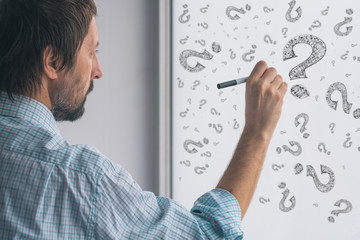 Perplexed businessman drawing question marks on whiteboard
