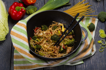 Spicy noodles with meat and vegetables in frying pan, next to fresh cabbage, peppers and onions