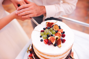 Newlyweds cut wedding cake decorated with raspberries and figs