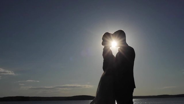 Silhouetted couple in love embrace and enjoy intimate moment together sky background contrast shadow evening sun shine light beams. Man woman backlit hold each other kiss copy space. Believing in love