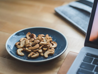 Some cashew nuts on small snack dish on work desk.