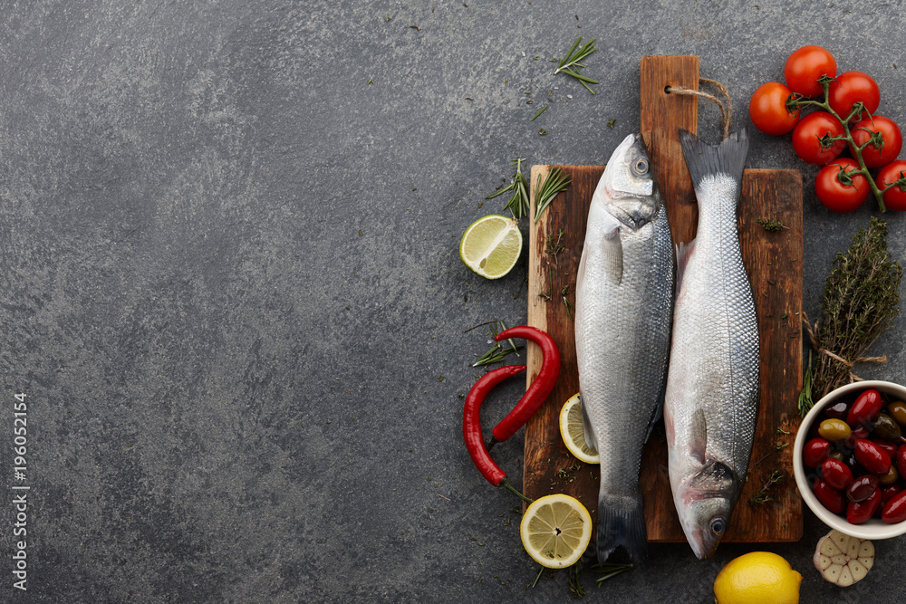 Poster fresh raw seabass on cutting board with ingredients. top view, copyspace.