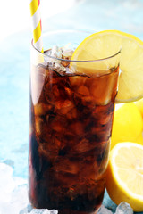 Softdrink with ice cubes, lemon and straw in glass.