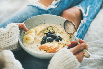 Healthy winter breakfast in bed. Woman in woolen sweater and shabby jeans eating vegan almond milk...