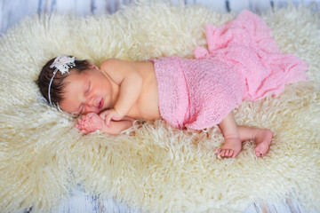sweet newborn baby sleeps on a pink  and white blanket on a wooden background.