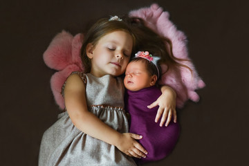 Little sister hugging her newborn sister. Toddler kid meeting new sibling. Cute girl and new born baby girl. Family with children at home. Love, trust and tenderness