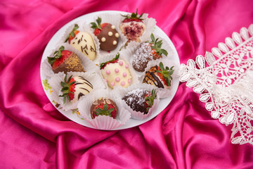 plate of Strawberries in white and milk chocolate on a pink silk background