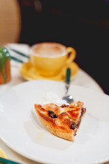 Piece of fresh tasty cake with walnuts on white plate. Yellow cup with hot coffee on background.