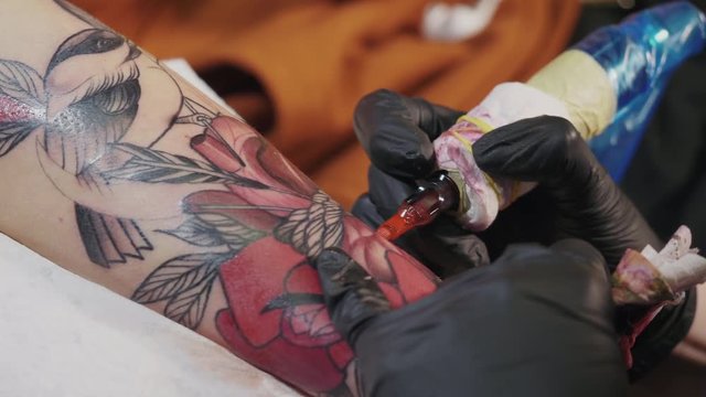 The tattoo artist at work. A girl holding a machine and applied in colorful picture on skin. the master of tattoos. Abstract pattern red ink flowers. 4k