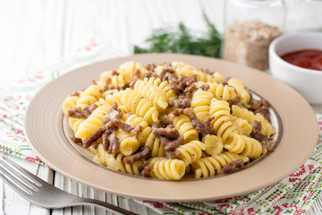 Fusilli pasta with minced meat and onion in navy-style on white wooden table. Makarony po-flotski, Russian dish.