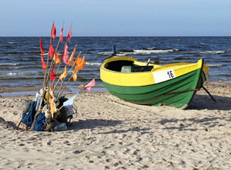 Green-yellow fishing boat and nets with flags on the sea shore.