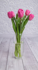 bouquet of pink fresh tulips in a glass vase on a gray background